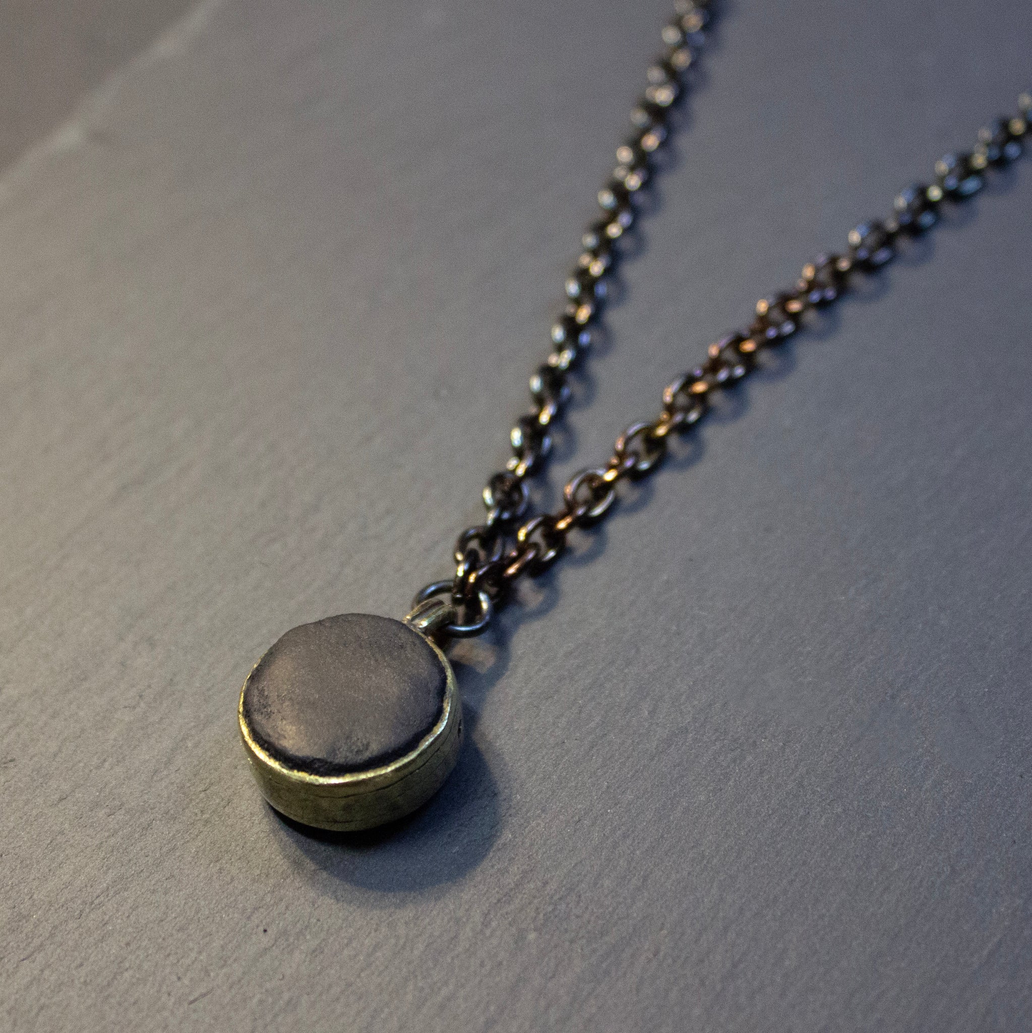 Leather and brass pendant on black chain. This pendant features a leather core, wet moulded and held in place via brass pins. The chain has been treated so that it has slight variations of colour, from warm bronze to black